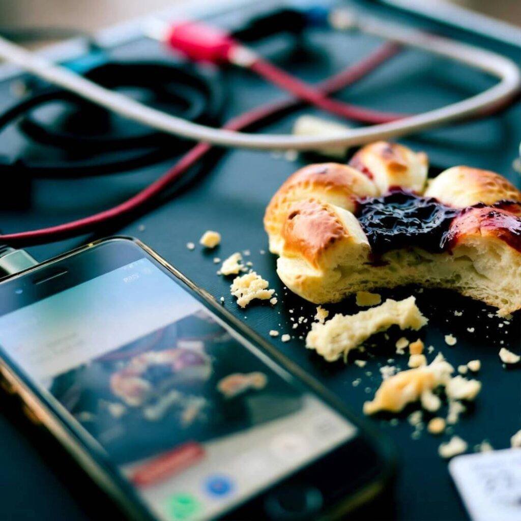 Blurry phone snap: folding table, tangled cables, half-eaten kolache.